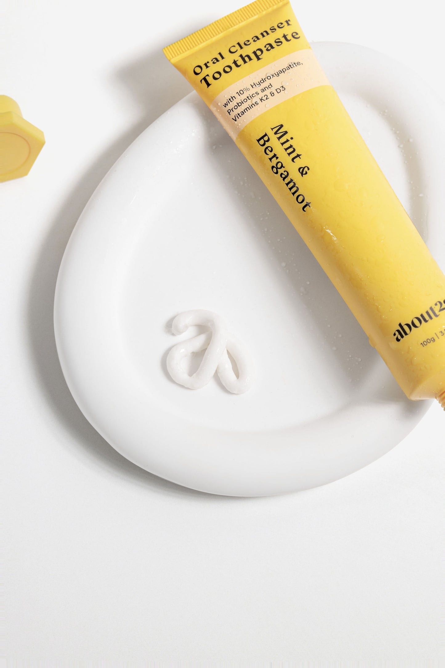 natural hydroxyapatite toothpaste tube on a dish with a toothpaste on the side, brand is About28 Oral Cleanser, mint and bergamot flavour fluoride-free