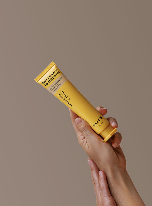hands holding a natural hydroxyapatite toothpaste yellow tube, brand is About28 Oral Cleanser, mint and bergamot flavour fluoride-free
